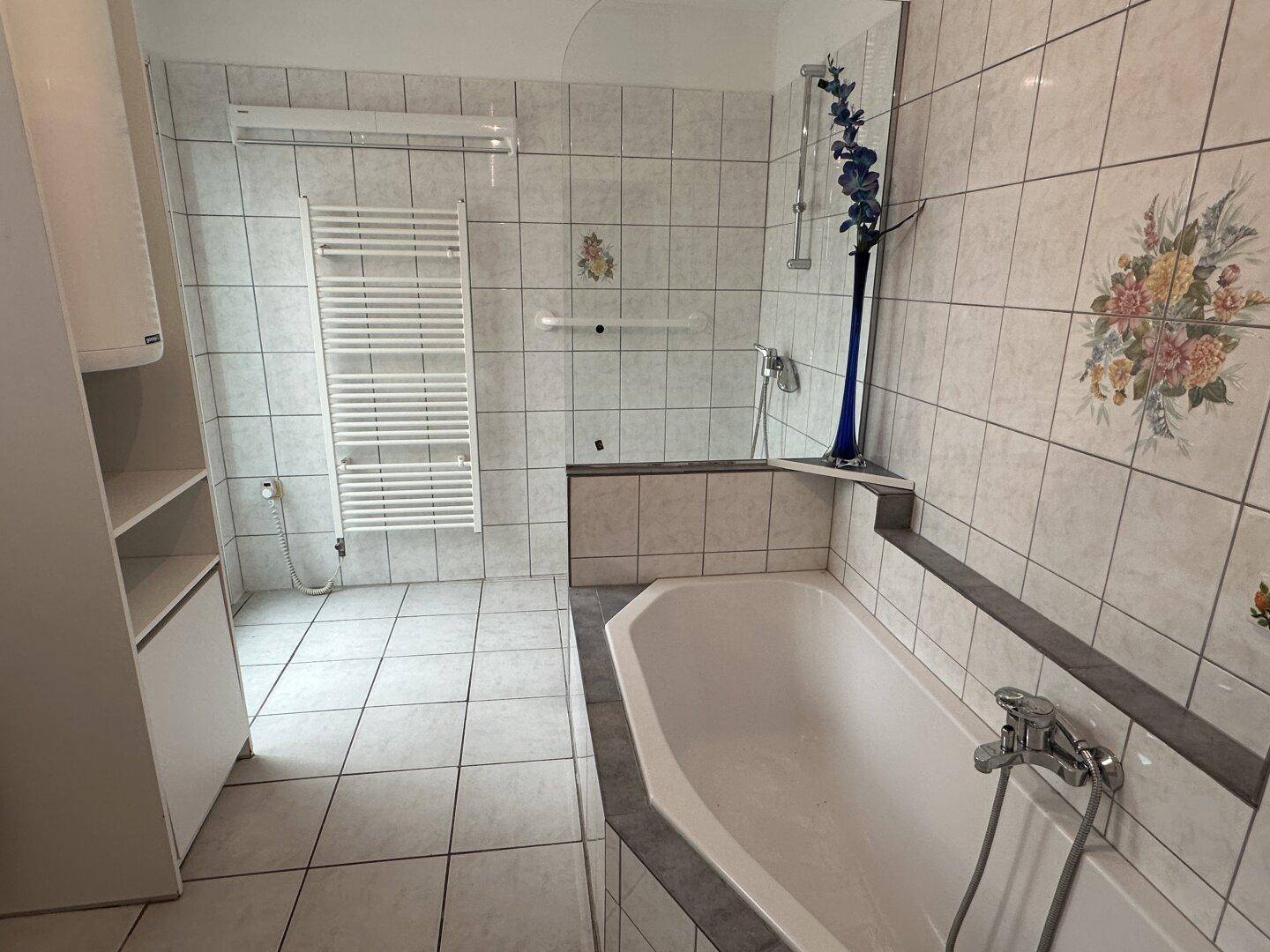 Badezimmer mit weißen Fliesen, Eckbadewanne, Duschbereich und beheiztem Handtuchhalter.