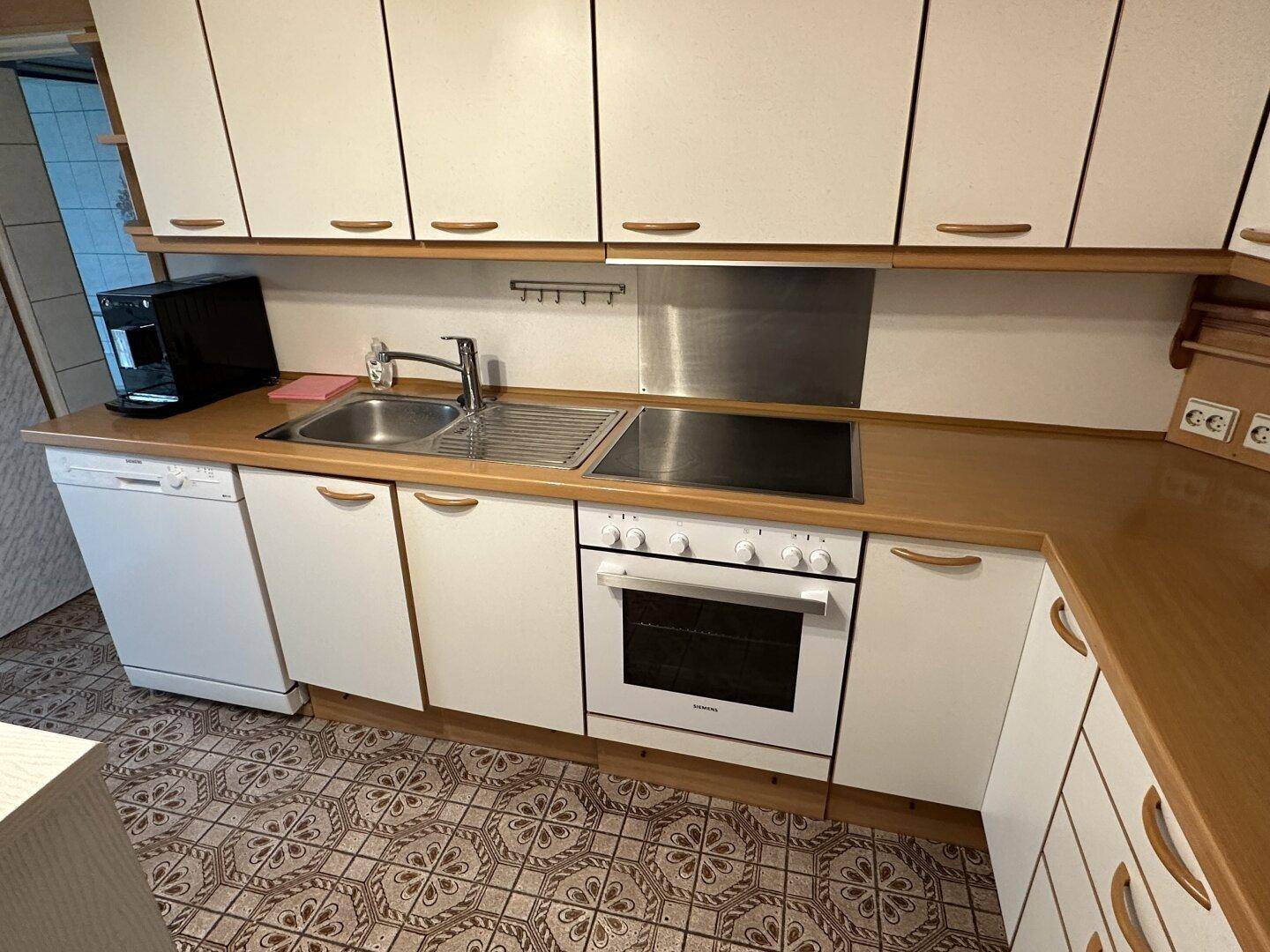 Küche mit weißen Schränken, Holzarbeitsplatten, Spüle, Kochfeld, Backofen und Geschirrspüler.