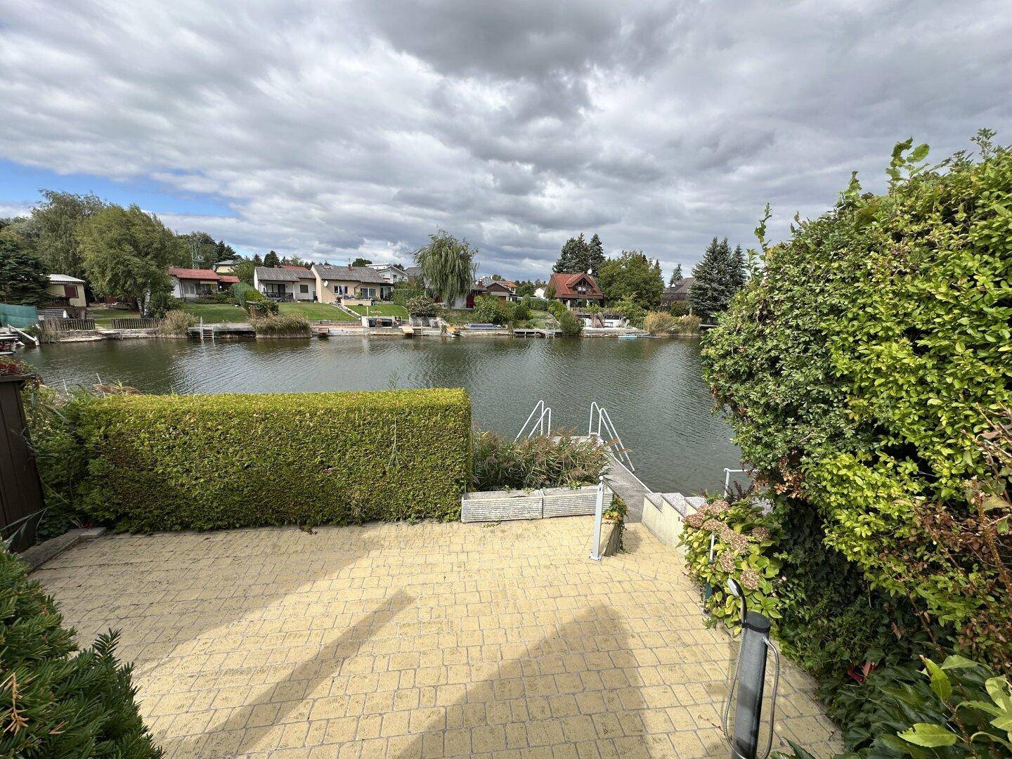 Gepflasterte Terrasse mit Hecke und Blick auf den Kanal sowie die umliegenden Häuser.