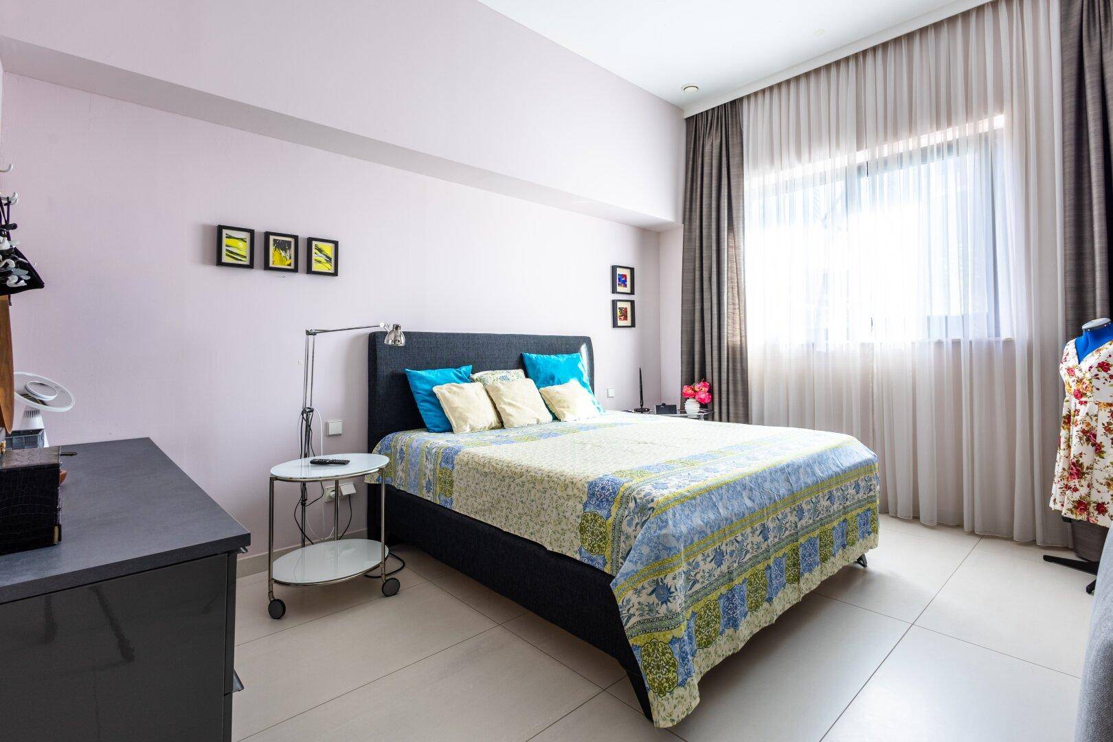Gemütliches Schlafzimmer mit hellem Bett, großen Fenstern und zarten Farbakzenten.