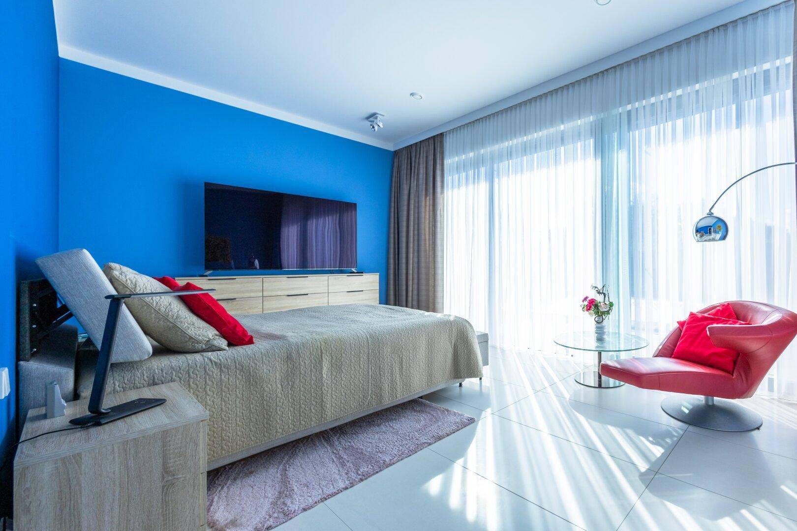 Helles Schlafzimmer mit blauen Wänden, großem Fenster und modernem Mobiliar.