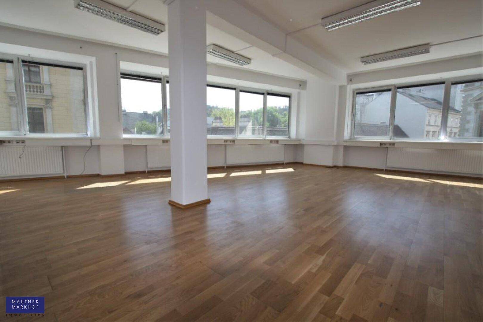 Geräumiges, leeres Büro mit vielen Fenstern, die einen weiten Blick und viel Tageslicht bieten.