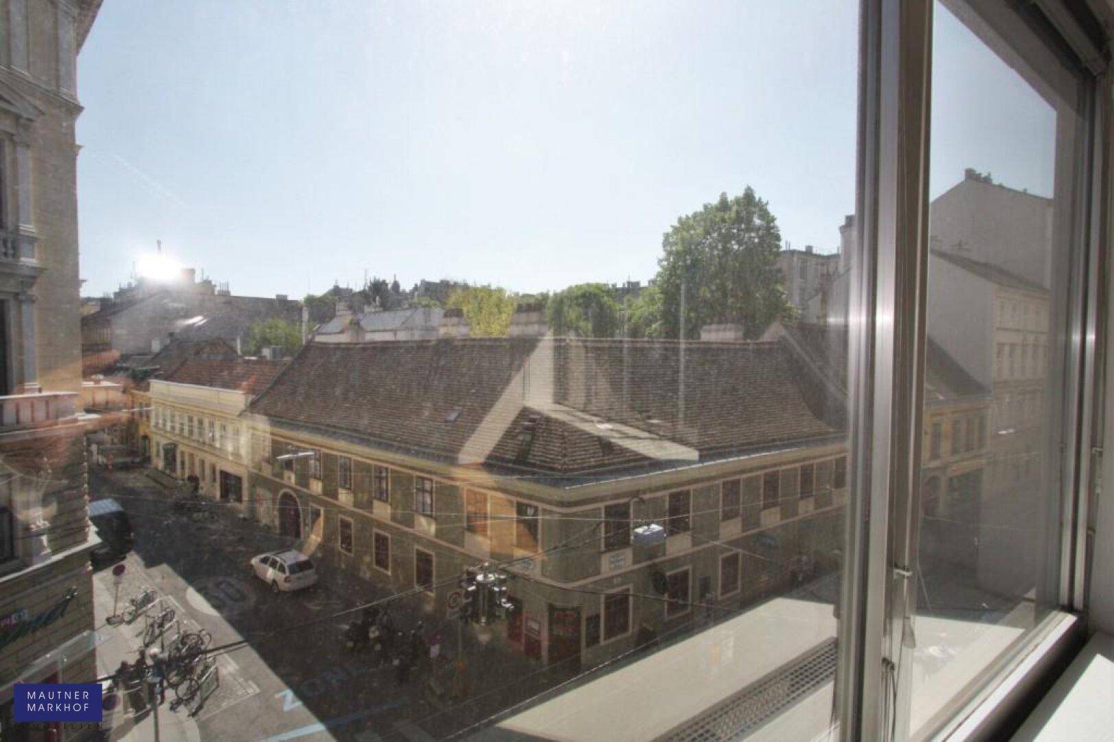 Blick aus einem Fenster eines Büros auf eine belebte Straße mit historischen Gebäuden und viel Tageslicht.