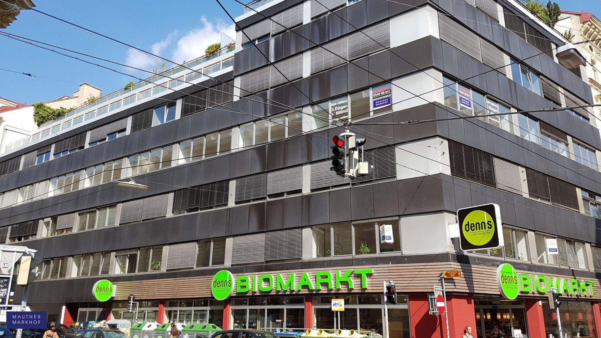 Modernes Geschäftsgebäude mit dunkler Fassade, großen Fenstern und einem Biomarkt im Erdgeschoss.