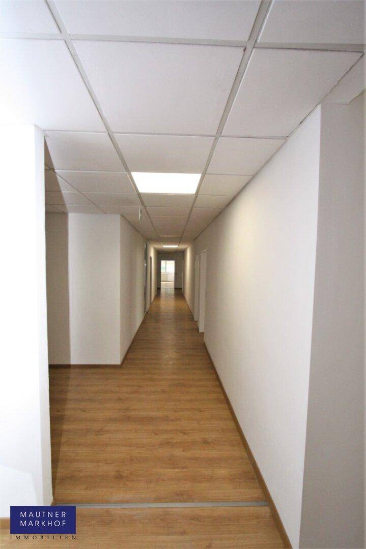 Schlichter, heller Flur mit Holzboden und abgehängter Decke, der zu weiteren Räumen führt.