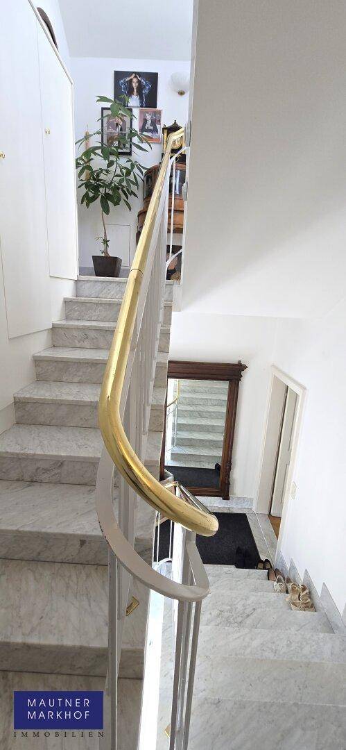 Elegante Marmortreppe mit goldenem Handlauf und modernen Kunstwerken an der Wand.