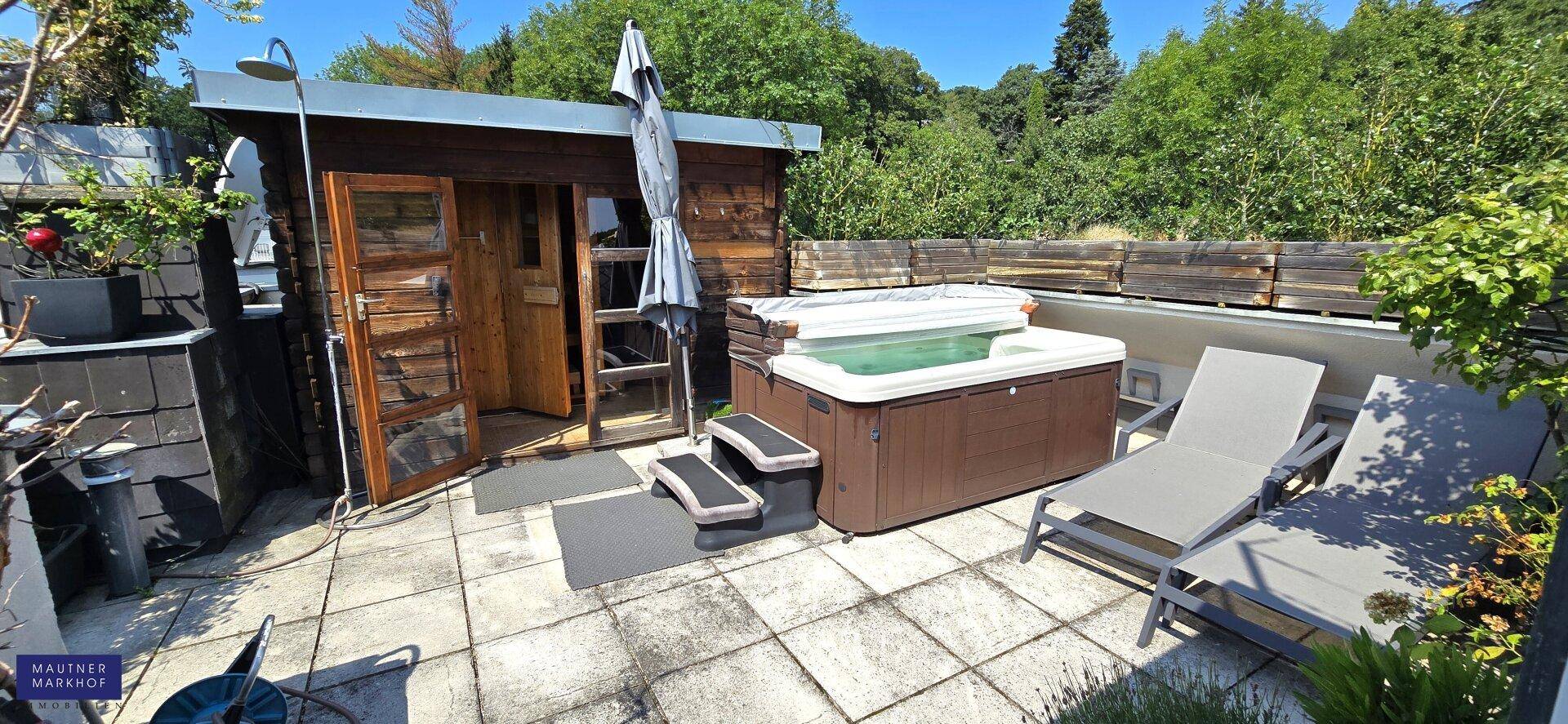 Große Terrasse mit Whirlpool, Saunahaus und Liegestühlen, umgeben von üppigem Grün.