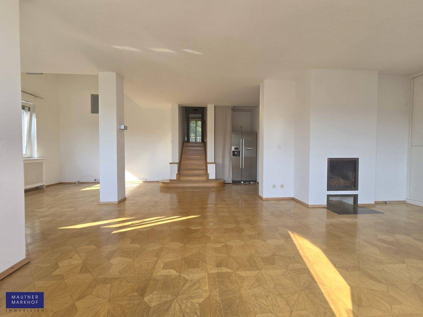 Geräumiger Wohnbereich mit Parkettboden, integriertem Kamin und offenem Übergang zur Treppe.