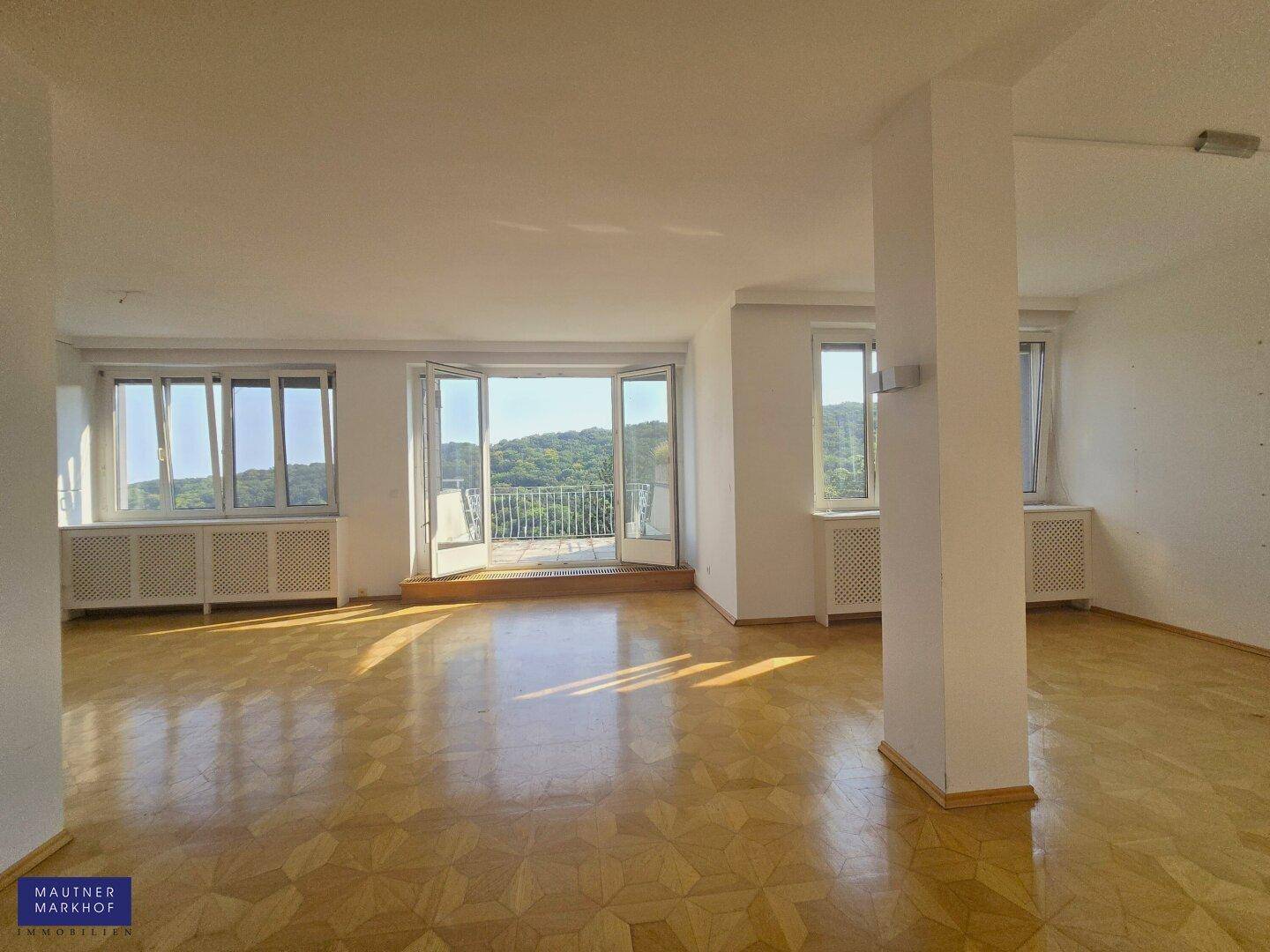 Helles Wohnzimmer mit Parkettboden, großen Fenstern und Zugang zu einem Balkon mit Grünblick.