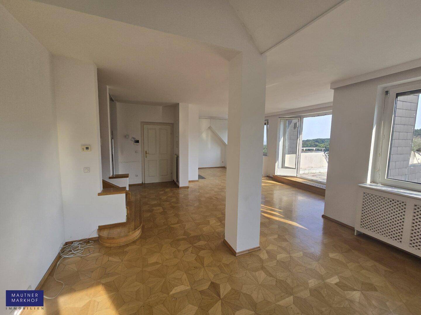 Heller Wohnbereich mit Parkettboden, Treppe und großen Fenstern, die viel Tageslicht hereinlassen.