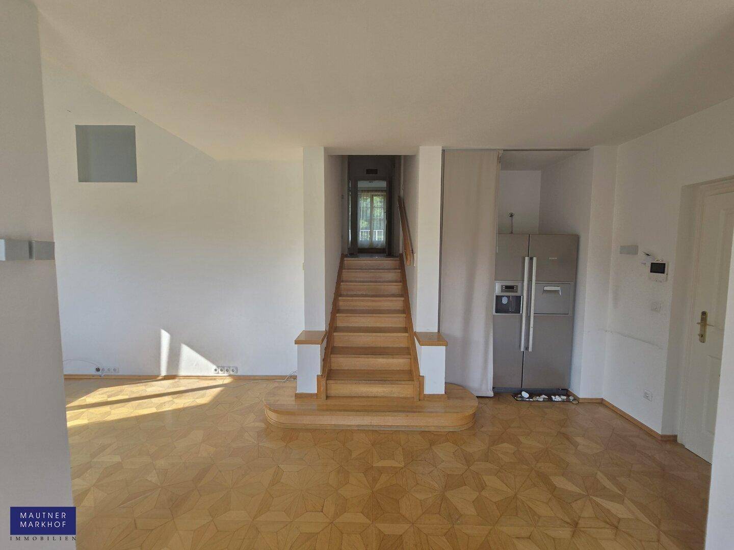 Offener Wohnbereich mit Holztreppe, integriertem Kühlschrank und viel natürlichem Licht.