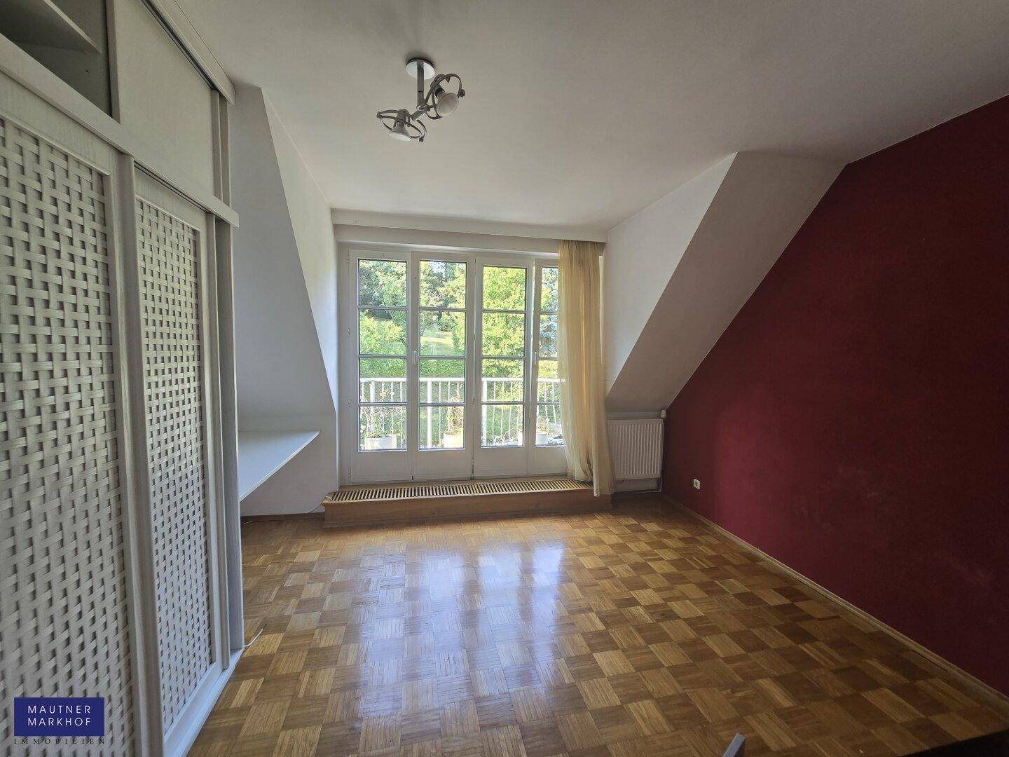 Schlafzimmer mit Dachschrägen, roter Akzentwand und Zugang zu einem französischen Balkon.