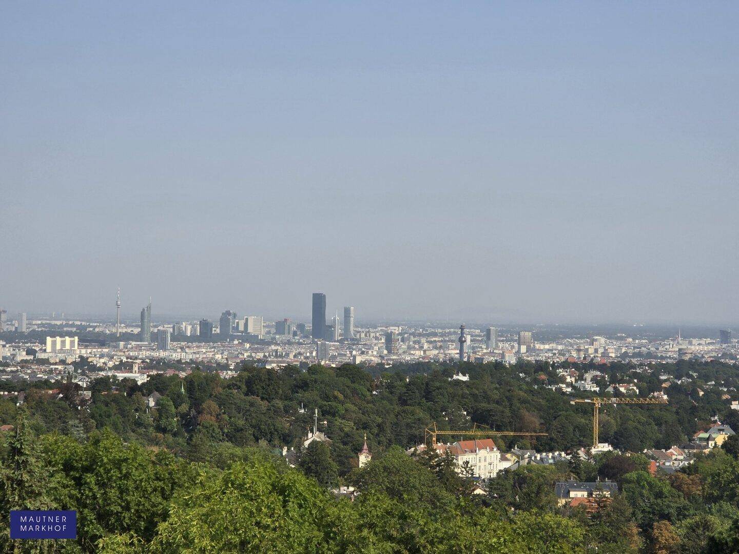 Panoramablick auf die Stadtlandschaft über grüne Hügel und Bäume an einem sonnigen Tag.
