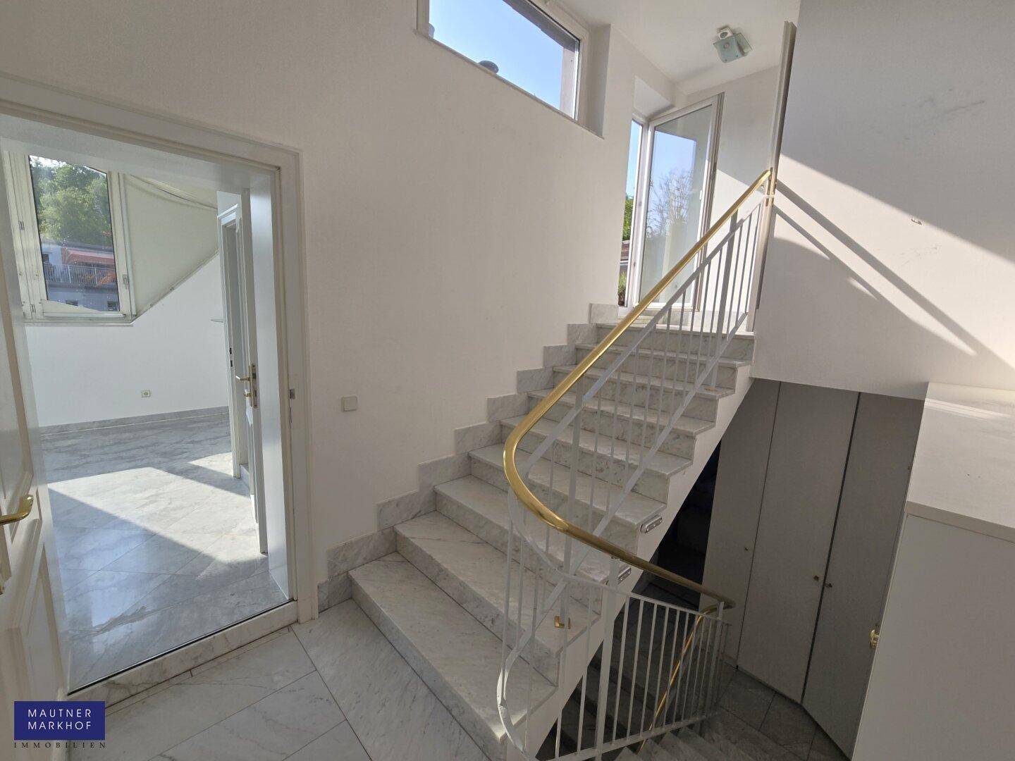 Elegante Marmortreppe mit Metallgeländer und natürlichem Lichteinfall, die die Etagen verbindet.