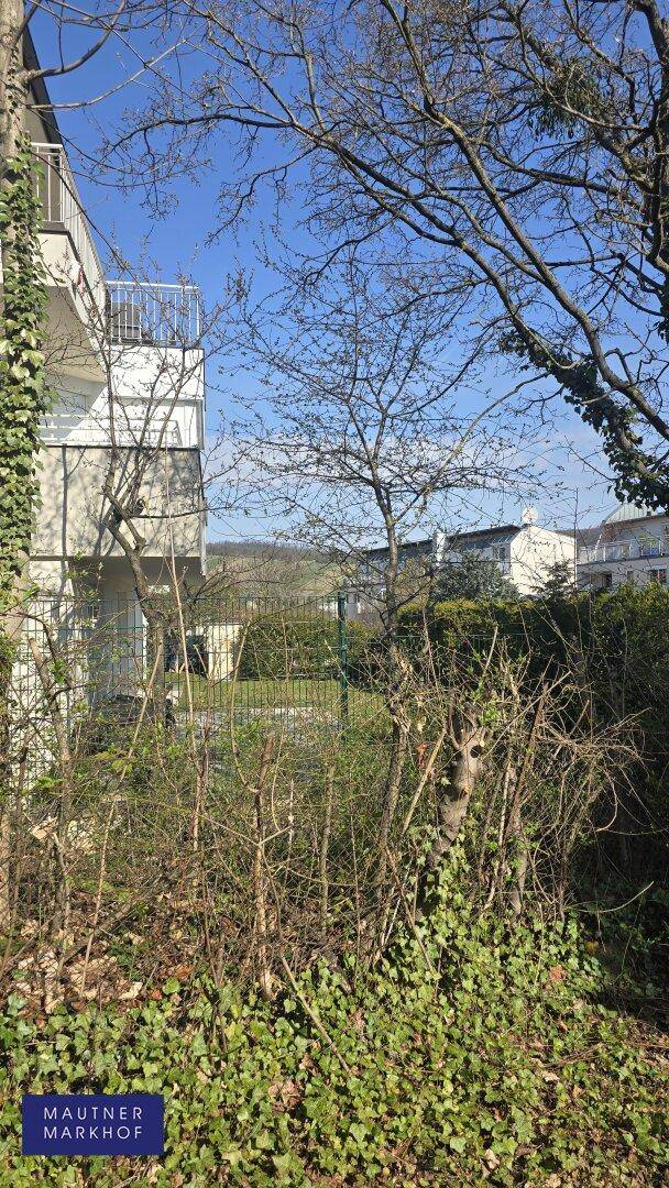 Außenansicht eines Gebäudes mit Balkon, umgeben von Bäumen und einem Zaun.