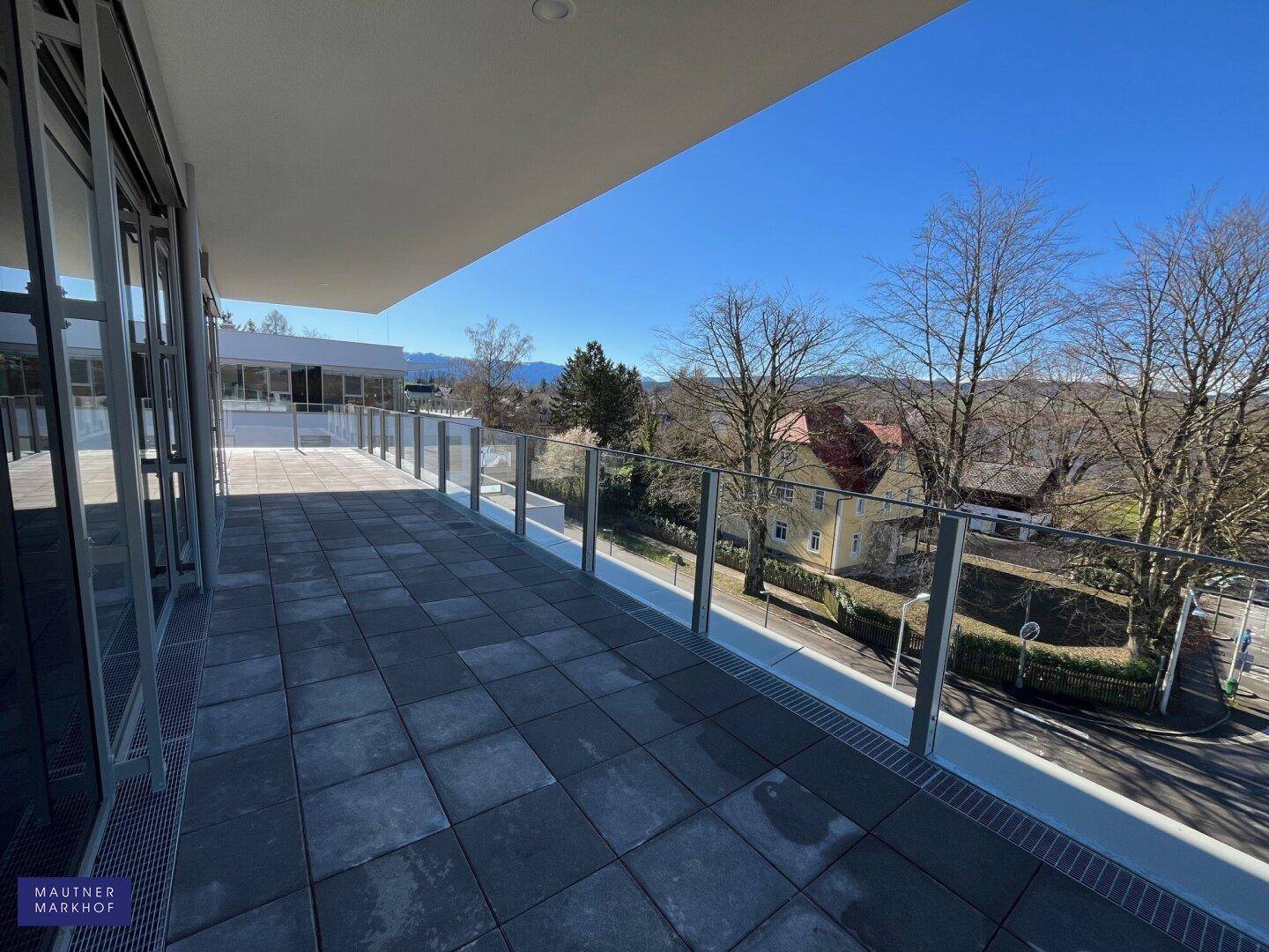 Sonnige Terrasse mit Glasgeländer und weitem Blick über die umliegende Nachbarschaft.