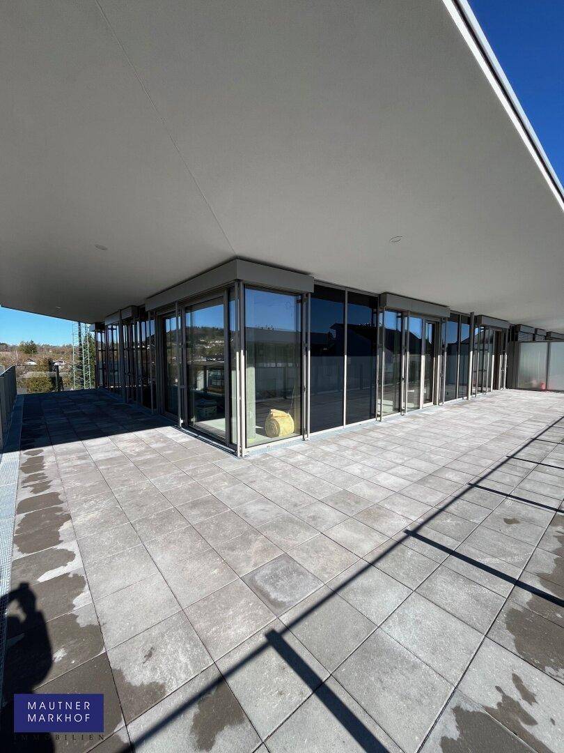 Moderne Terrasse mit großflächigen Fliesen und raumhohen Glasfronten des Gebäudes.