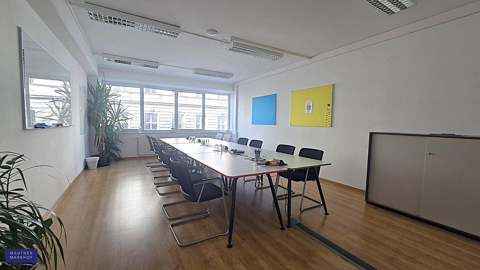 Konferenzraum mit langem Tisch und Stühlen, ausgestattet mit Pflanzen und großen Fenstern für natürliches Licht.