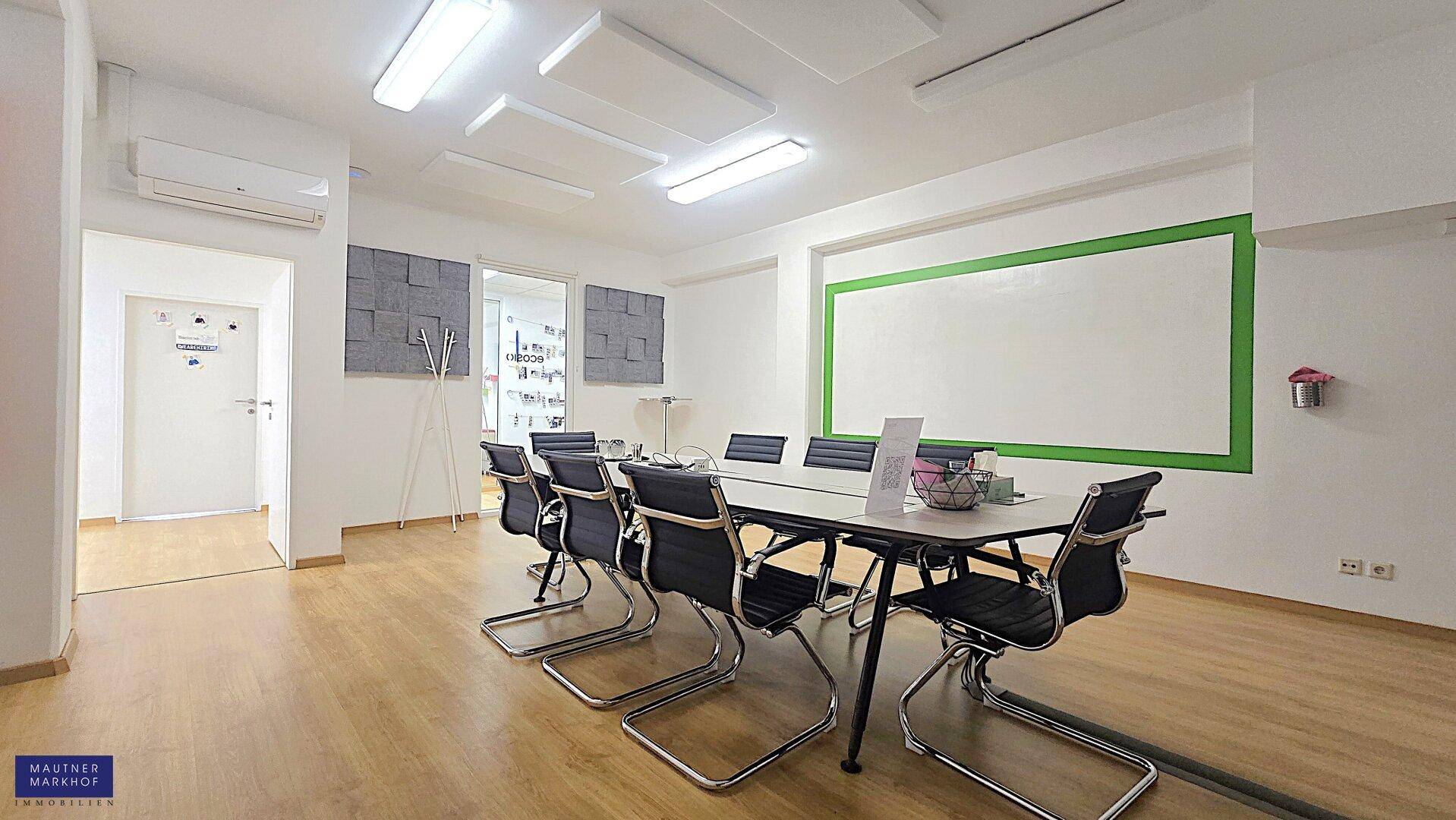 Konferenzraum mit großem Tisch und Stühlen, ausgestattet mit Whiteboard und schallabsorbierenden Deckenplatten.