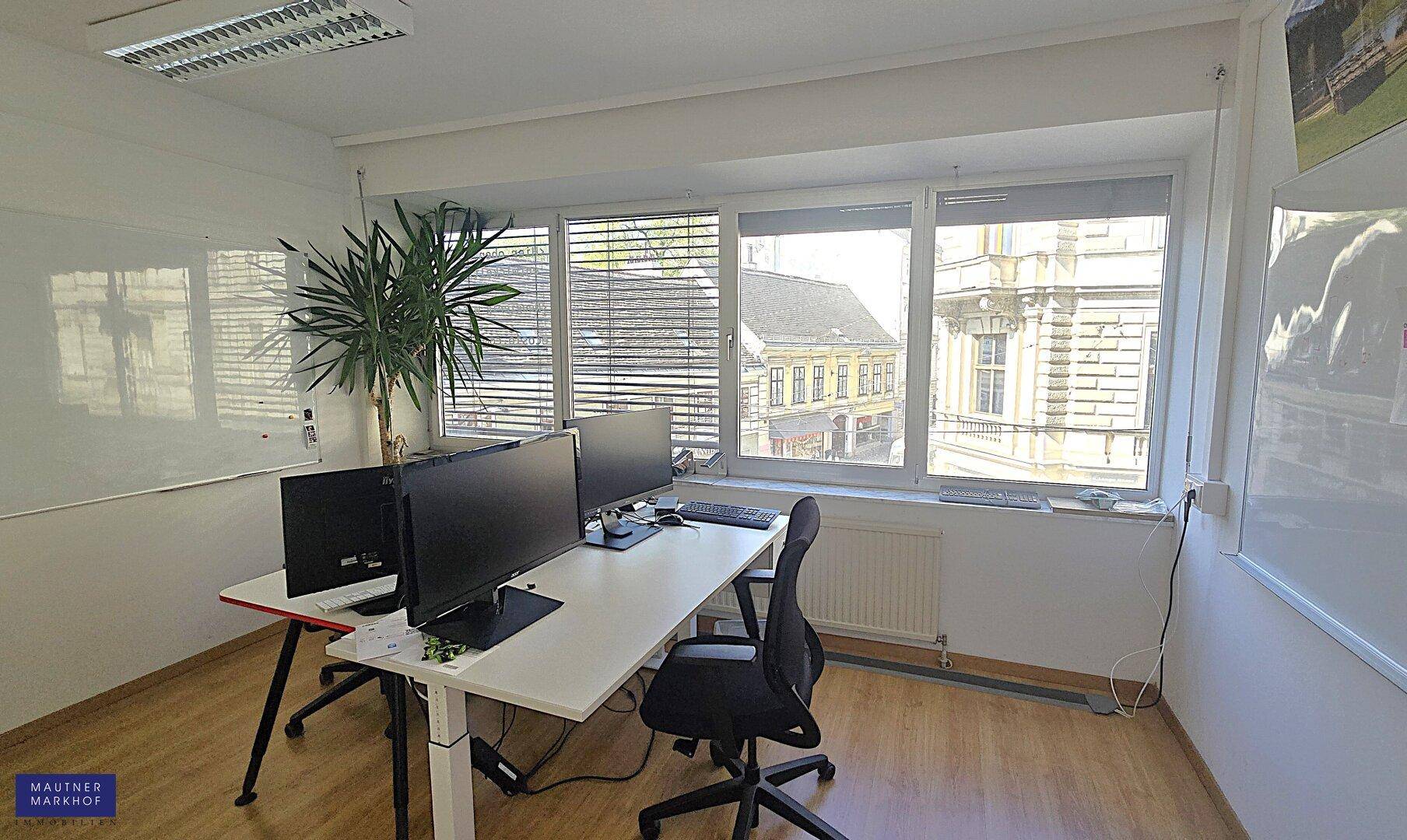 Büro mit Arbeitsplätzen, Computern und einem großen Fenster, das einen Blick auf die Straße bietet.