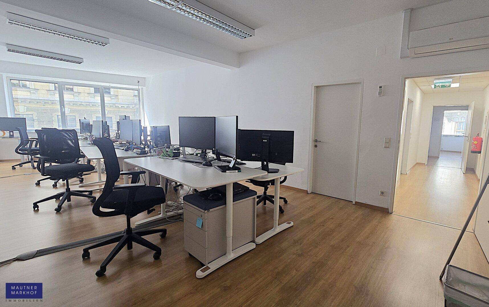 Büro mit mehreren Arbeitsplätzen, Computern und Bürostühlen, mit Klimaanlage und Zugang zu einem Flur.