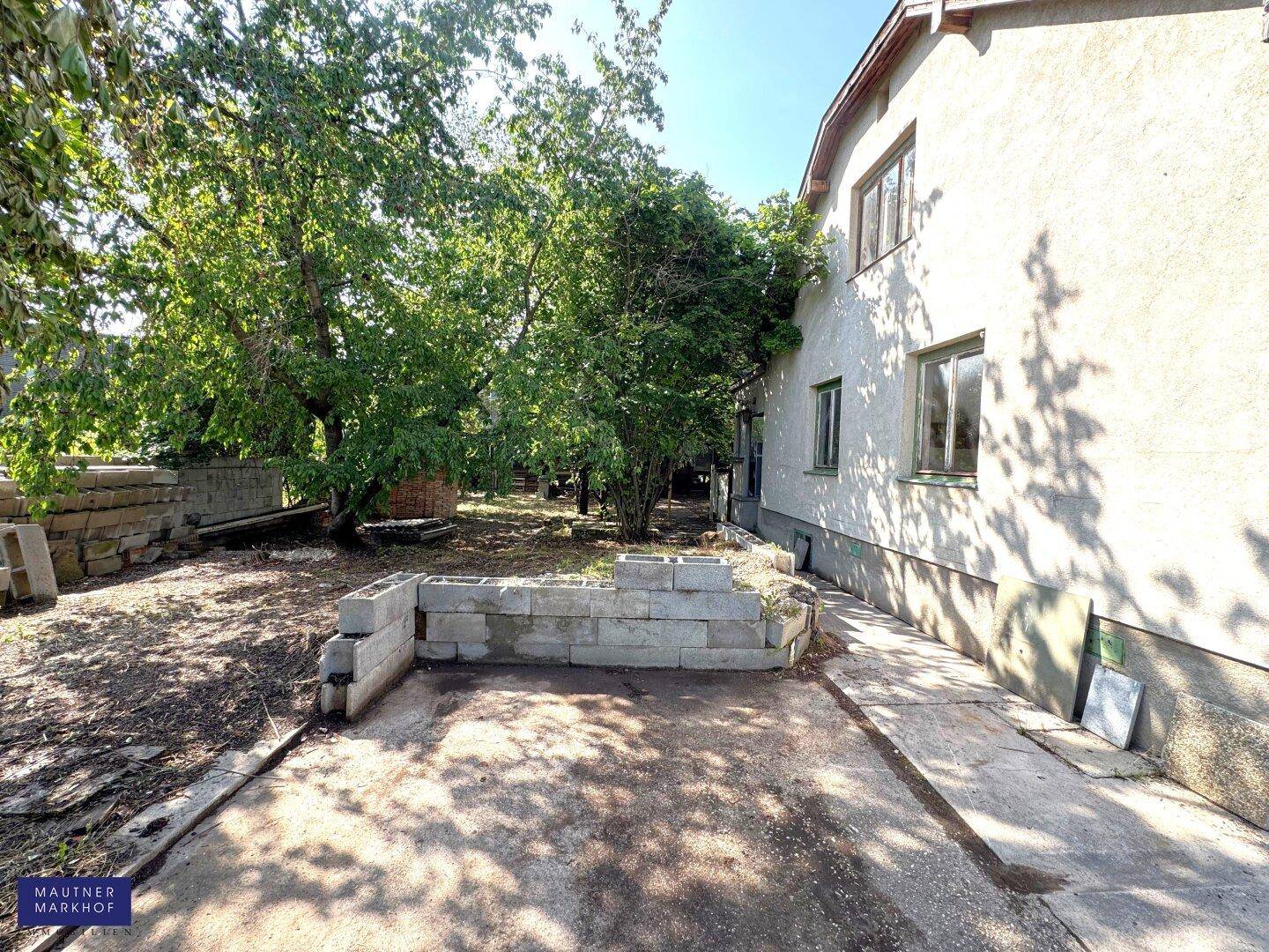 Seitenansicht des Hauses mit gepflastertem Weg und einem erhöhten Beet aus Betonsteinen.
