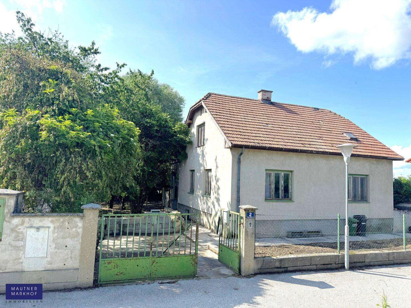 Einfamilienhaus mit rotem Ziegeldach, grüner Einfahrt und einem kleinen Vorgarten.