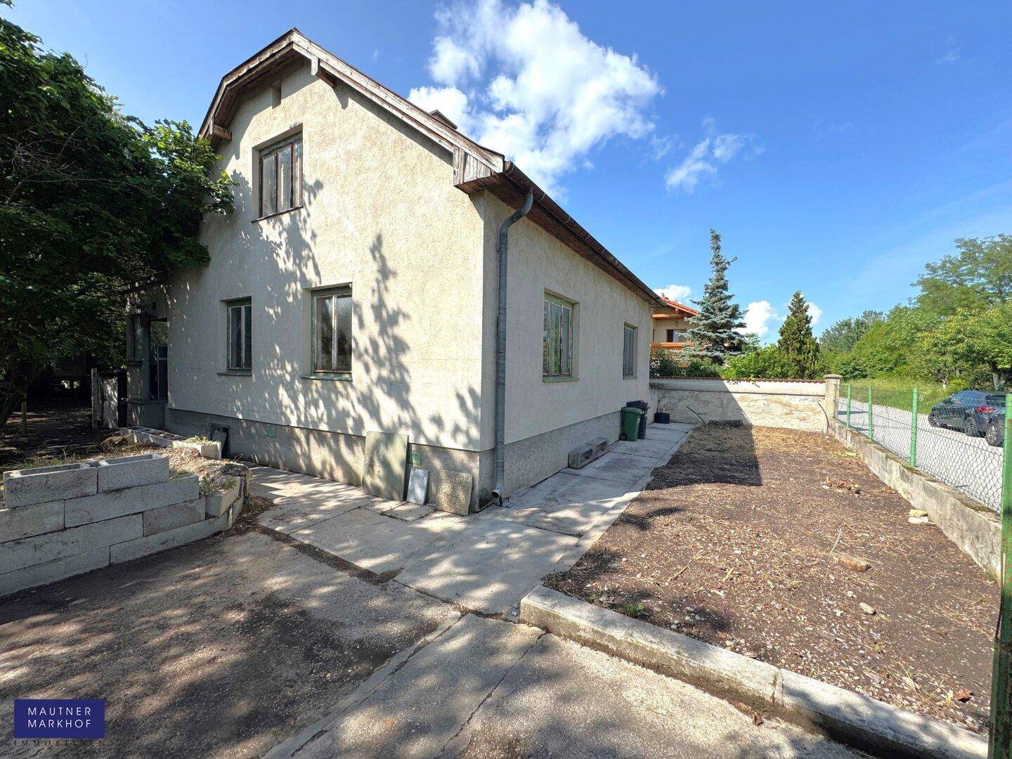 Seitenansicht des Hauses mit einfacher Fassade und einem ungestalteten Grundstücksbereich.