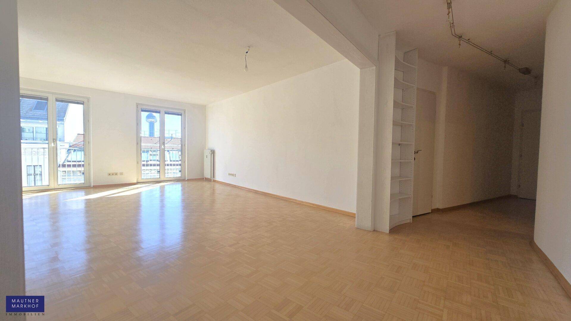 Geräumiger, heller Wohnbereich mit klassischem Parkettboden und Zugang zu zwei Balkonen.