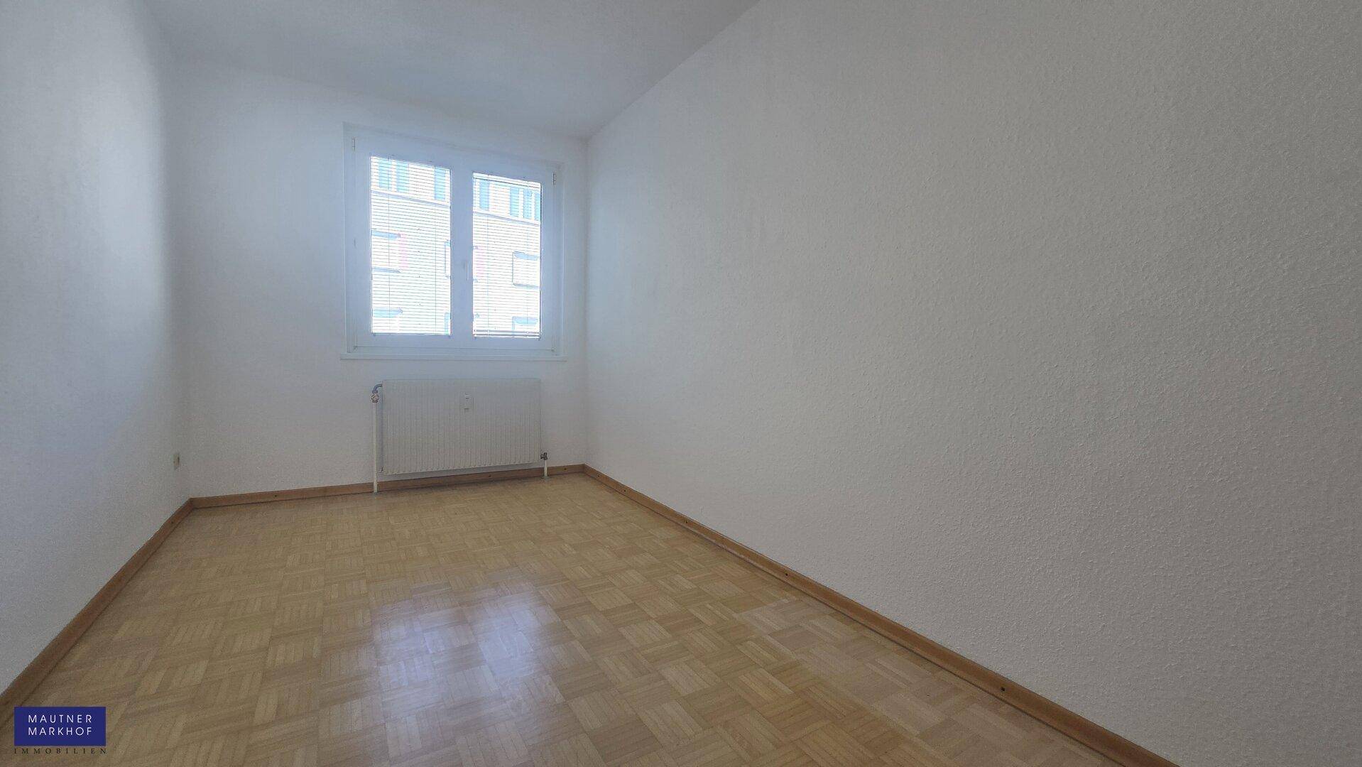 Weiteres Schlafzimmer mit Parkettboden und einem Fenster, das für eine angenehme Helligkeit sorgt.
