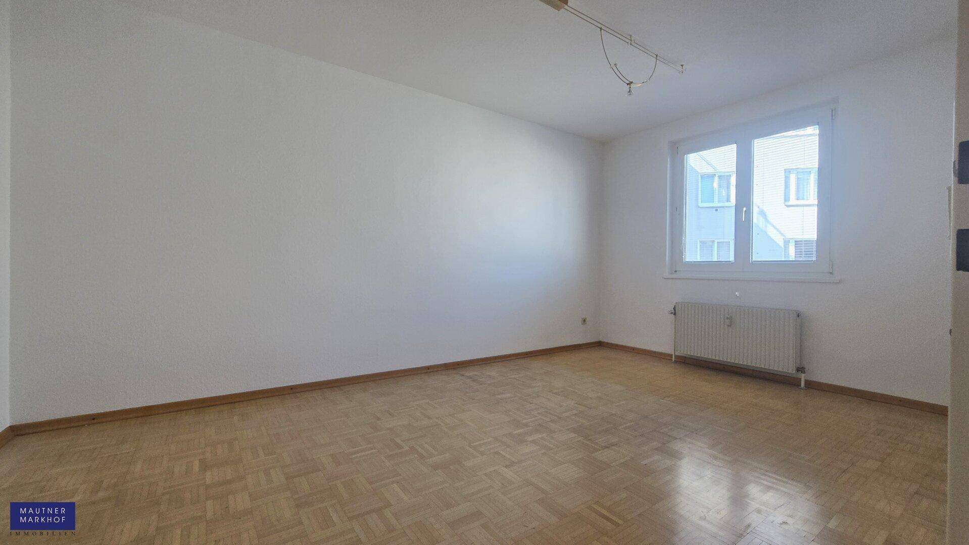 Helles Schlafzimmer mit Parkettboden und einem großen Fenster, das viel Tageslicht spendet.