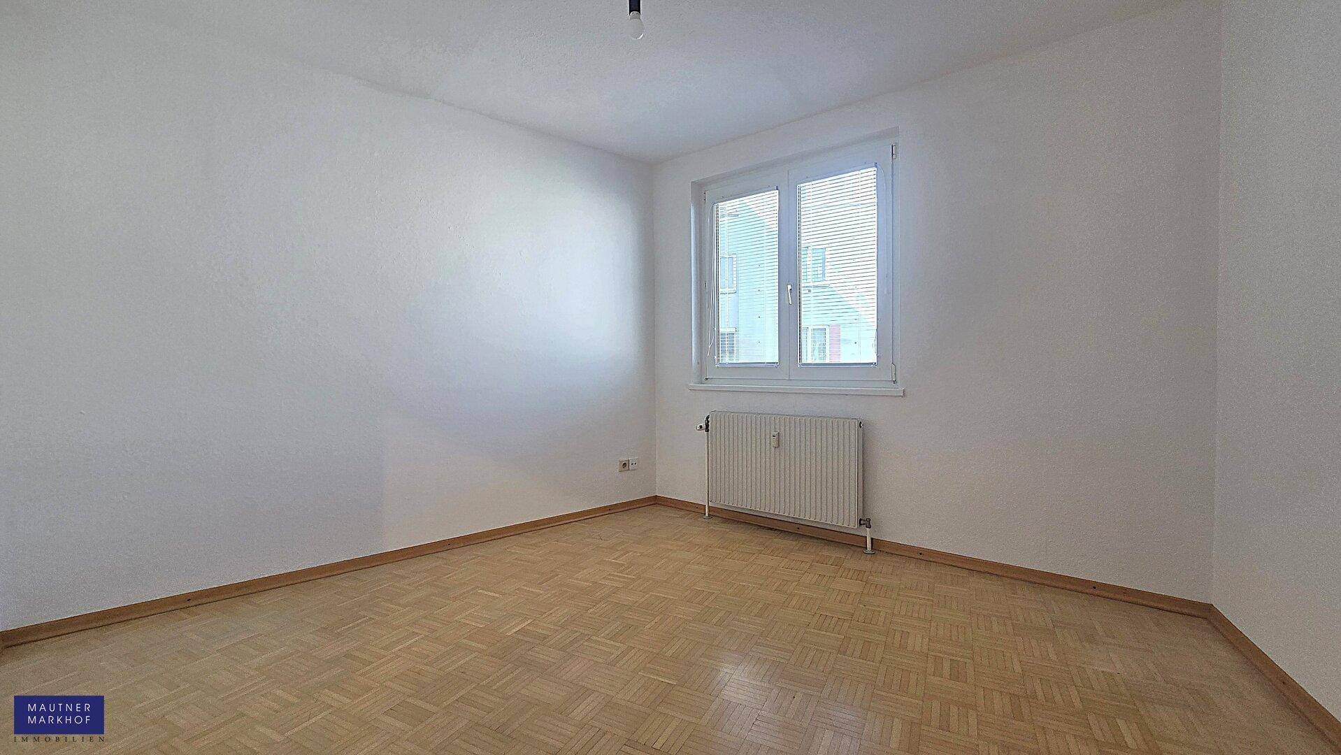 Ruhiges Schlafzimmer mit hellem Parkettboden und einem Fenster, das den Raum gut belichtet.