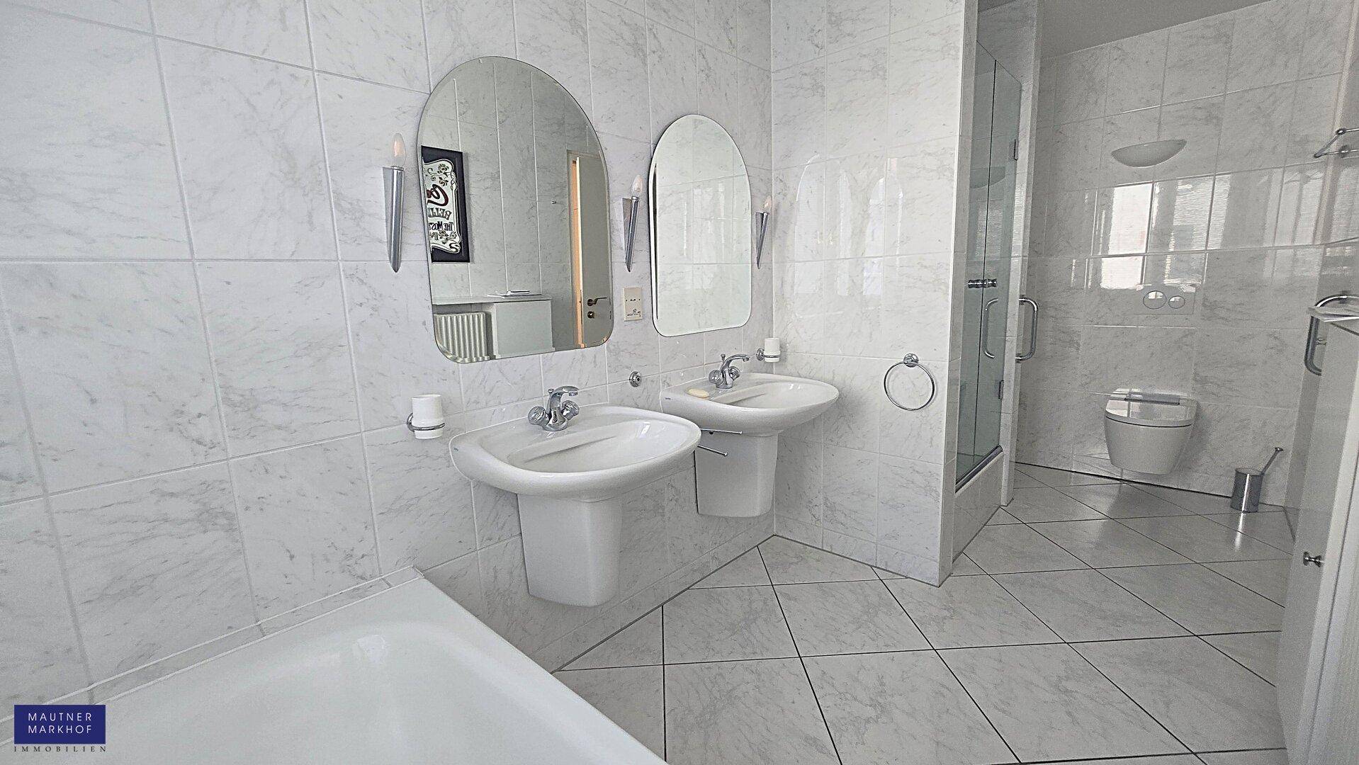 Geräumiges Badezimmer mit doppelten Waschbecken, Duschkabine, Badewanne und hellen Marmorfliesen.
