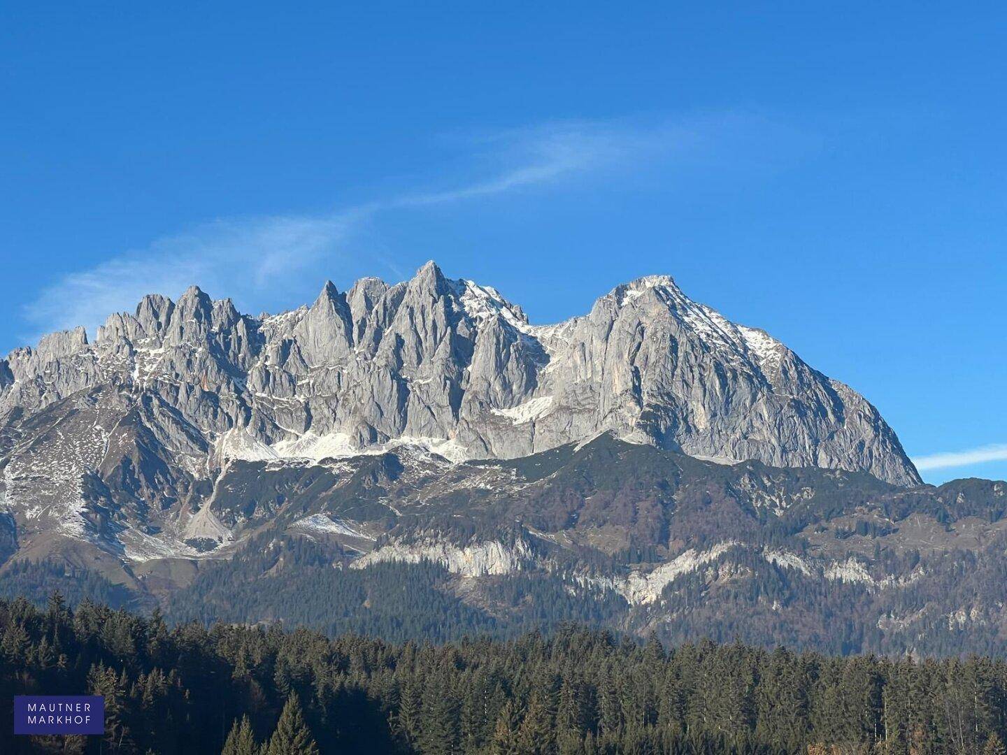 Majestätische Berglandschaft mit schneebedeckten Gipfeln und weitem Blick unter blauem Himmel.