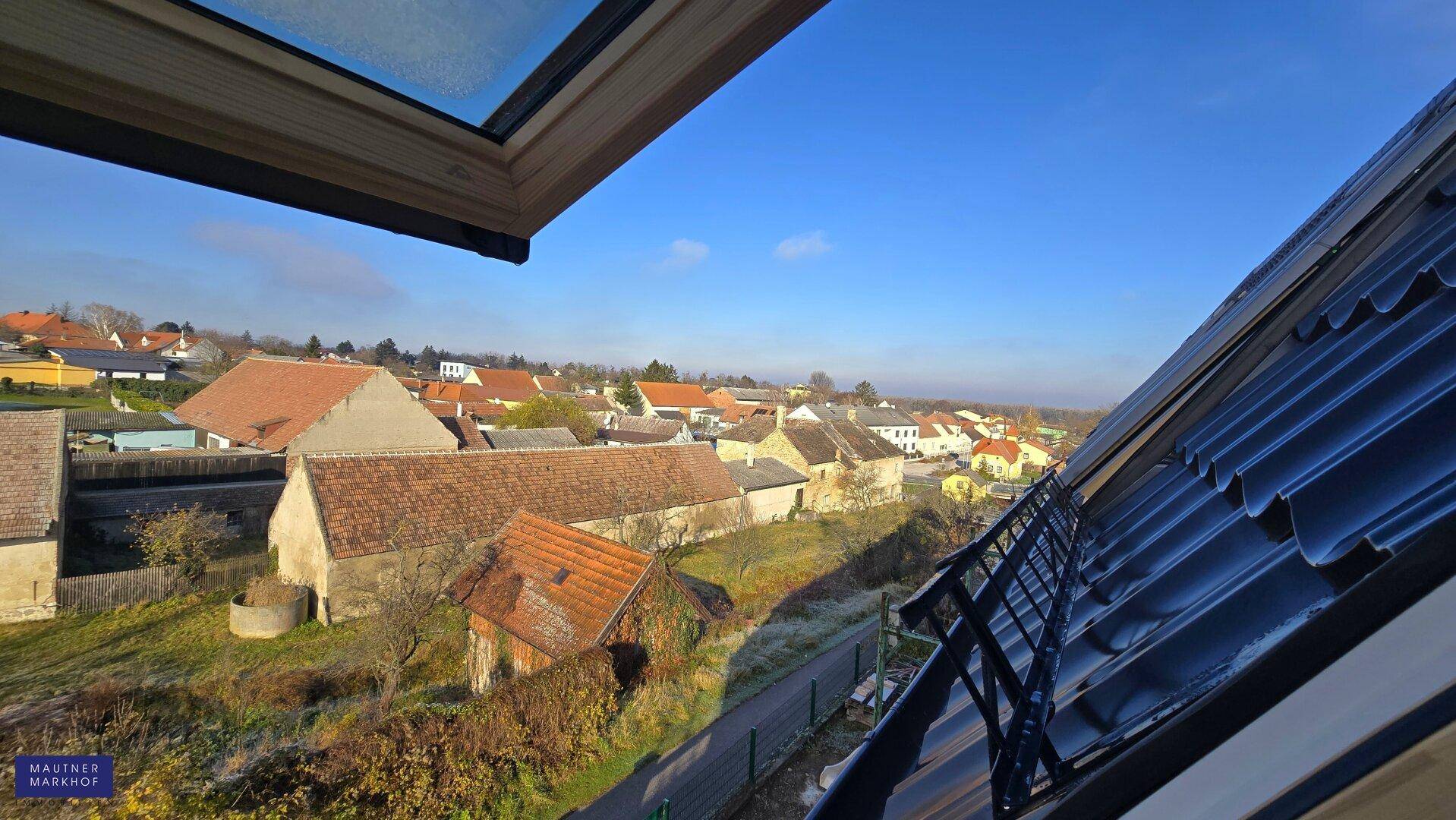 Blick aus einem Dachfenster auf die Dächer des Dorfes und die weite Landschaft.