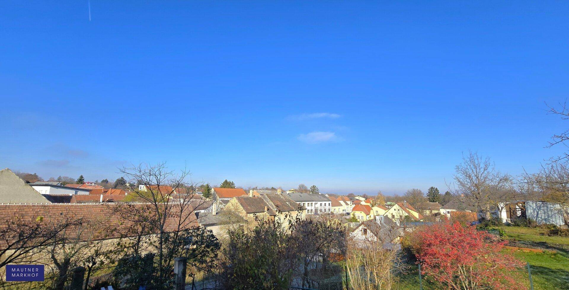 Weitläufiger Blick über die ländliche Umgebung mit Häusern und Feldern unter blauem Himmel.
