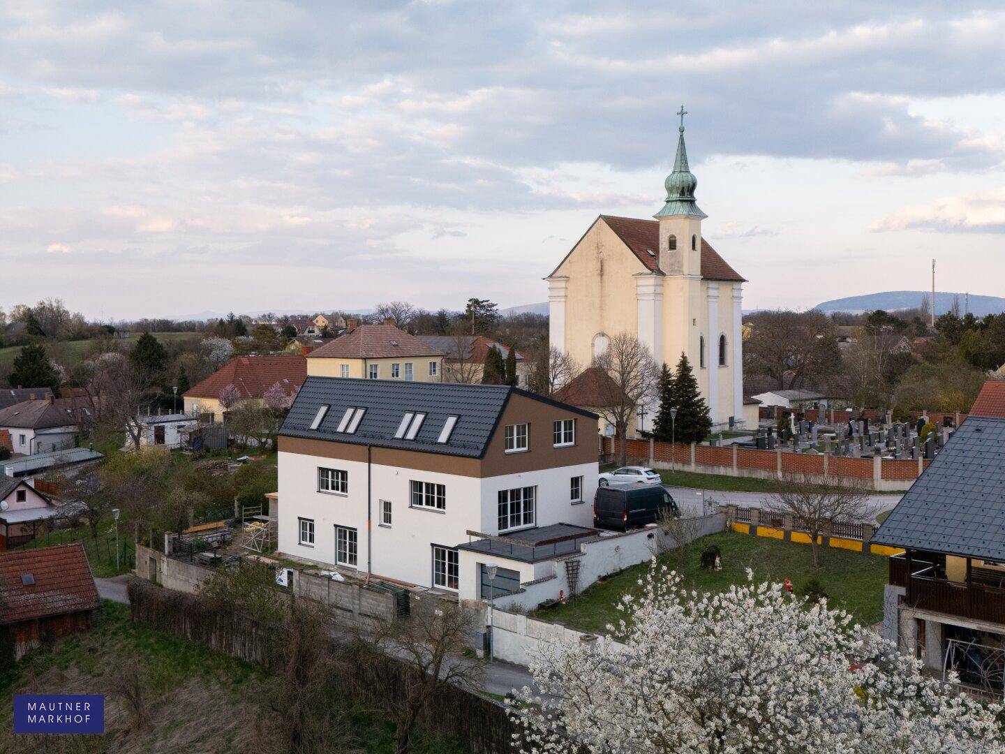 Luftaufnahme des Hauses mit angrenzender Kirche und Friedhof in einer ruhigen Wohngegend.