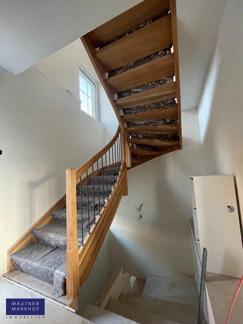 Holztreppe im Bau mit elegantem Geländer und natürlichem Lichteinfall durch ein Fenster.
