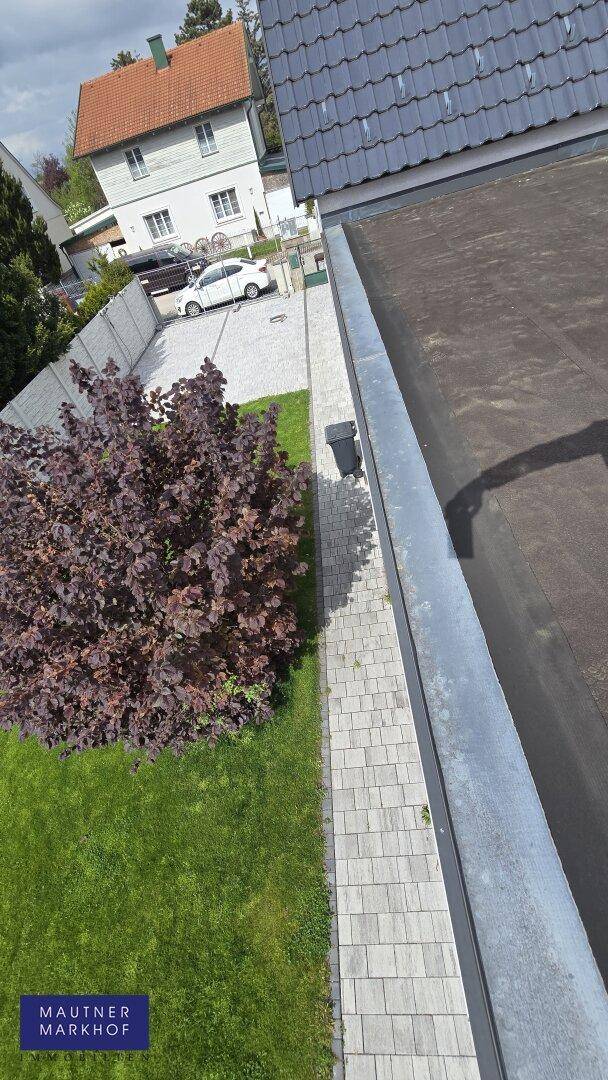 Seitenansicht des Hauses mit gepflastertem Weg, Rasenfläche und Flachdachbereich.