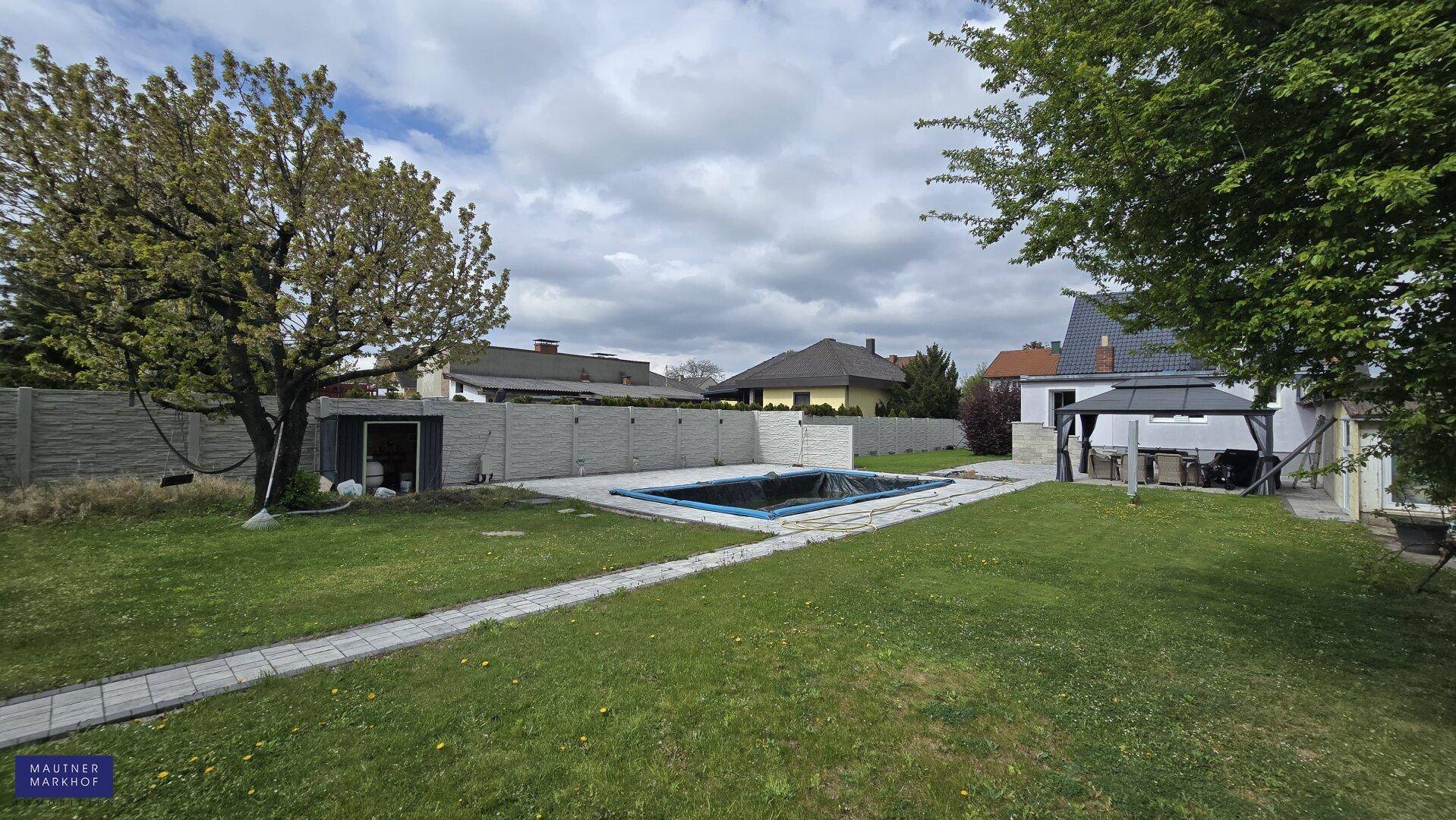 Großer Garten mit Pool, überdachtem Sitzbereich und weitläufiger Rasenfläche.