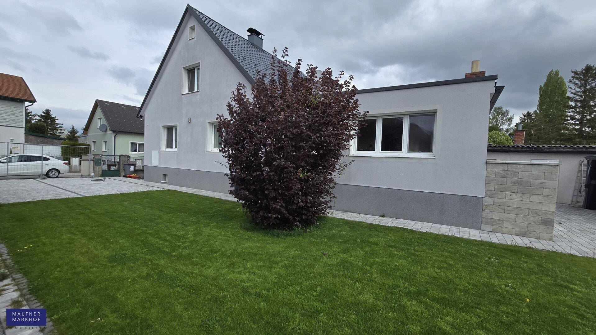Ansicht des Einfamilienhauses mit gepflegtem Vorgarten und Zufahrt unter bewölktem Himmel.