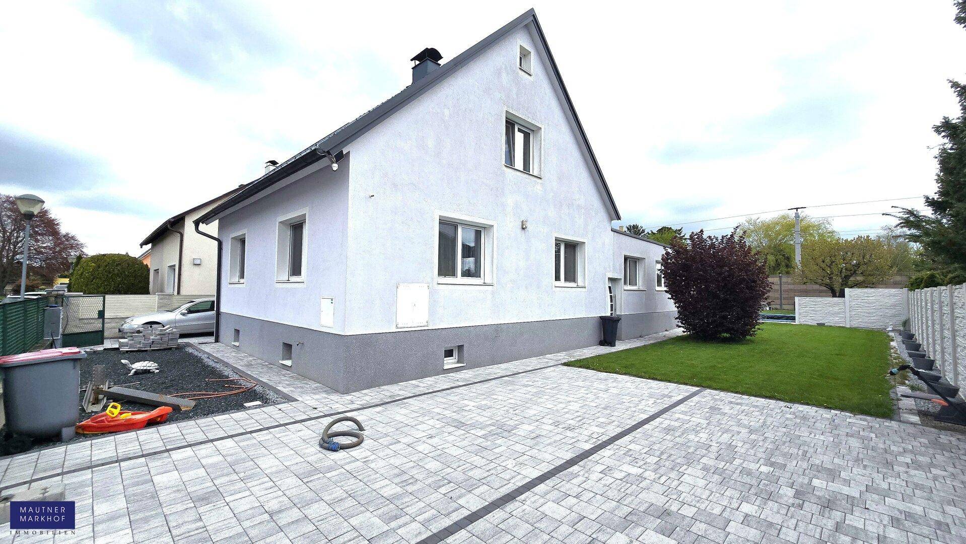 Seitenansicht des Hauses mit gepflasterter Zufahrt und vorbereitetem Gartenbereich.