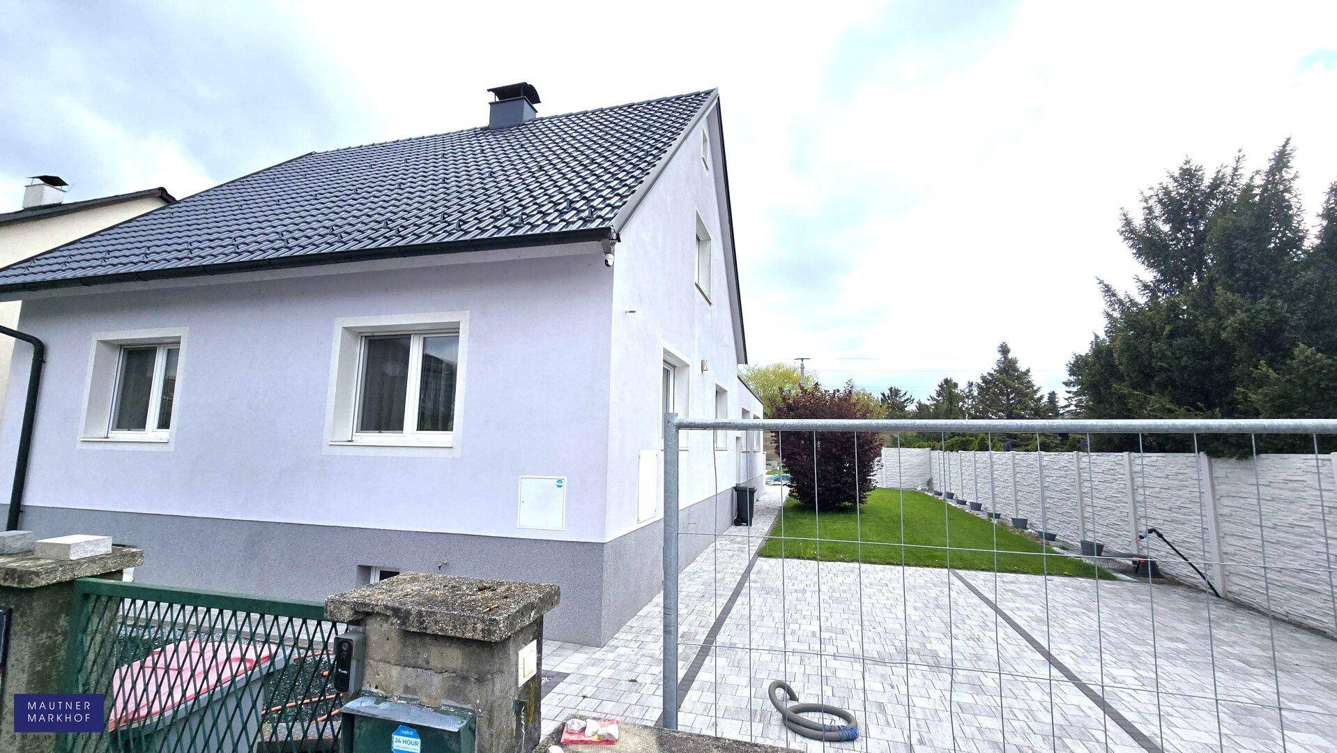 Seitenansicht des Hauses mit gepflegtem Garten und Zaun.