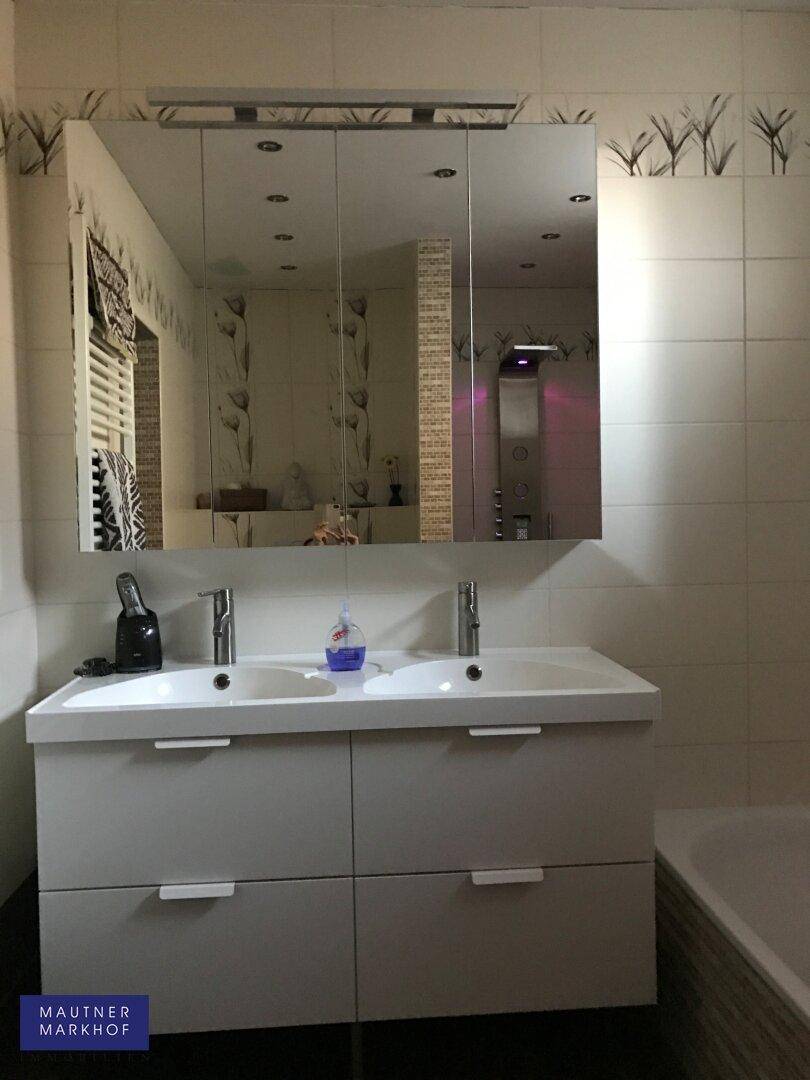 Helles Badezimmer mit Doppelwaschbecken, Spiegelschrank und modernen Fliesen.