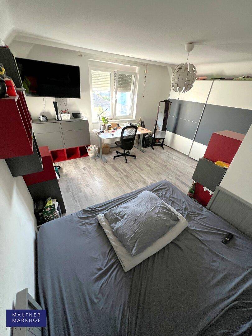 Jugendzimmer mit Bett, Schreibtisch und modernem Schrank mit Schiebetüren.