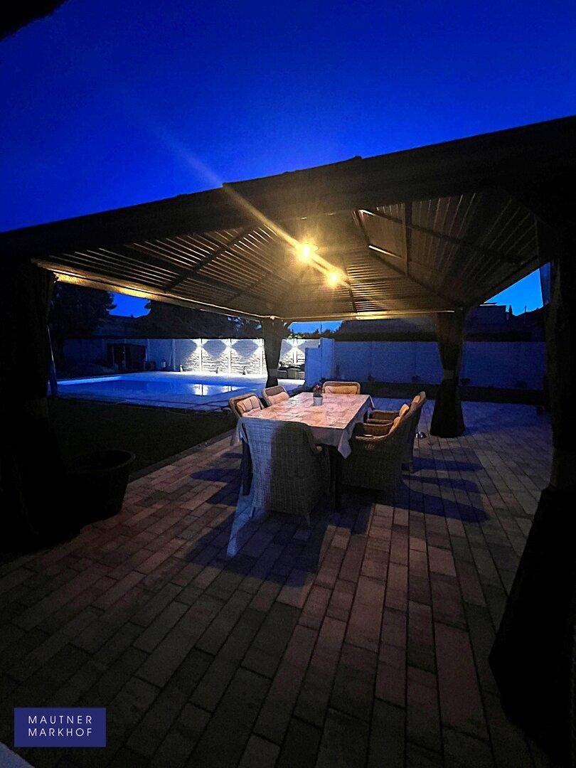 Beleuchteter überdachter Sitzbereich am Abend mit Blick auf den Pool.