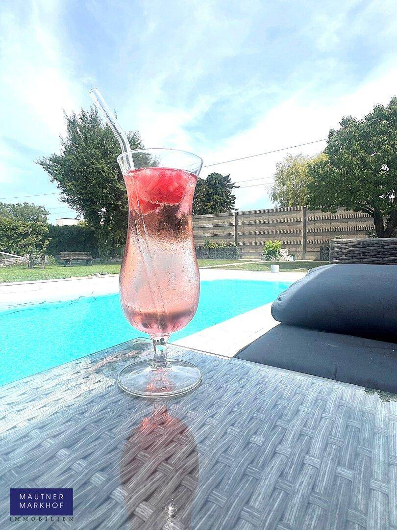 Erfrischender Poolbereich mit einem kühlen Getränk und bequemen Outdoor-Möbeln unter blauem Himmel.