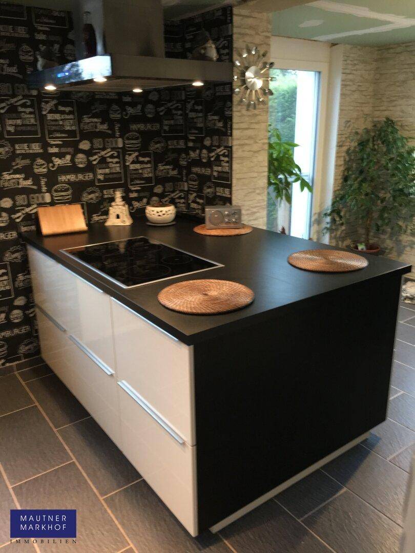 Moderne Kochinsel mit Induktionskochfeld und dunkler Arbeitsplatte in einer hellen Küche.