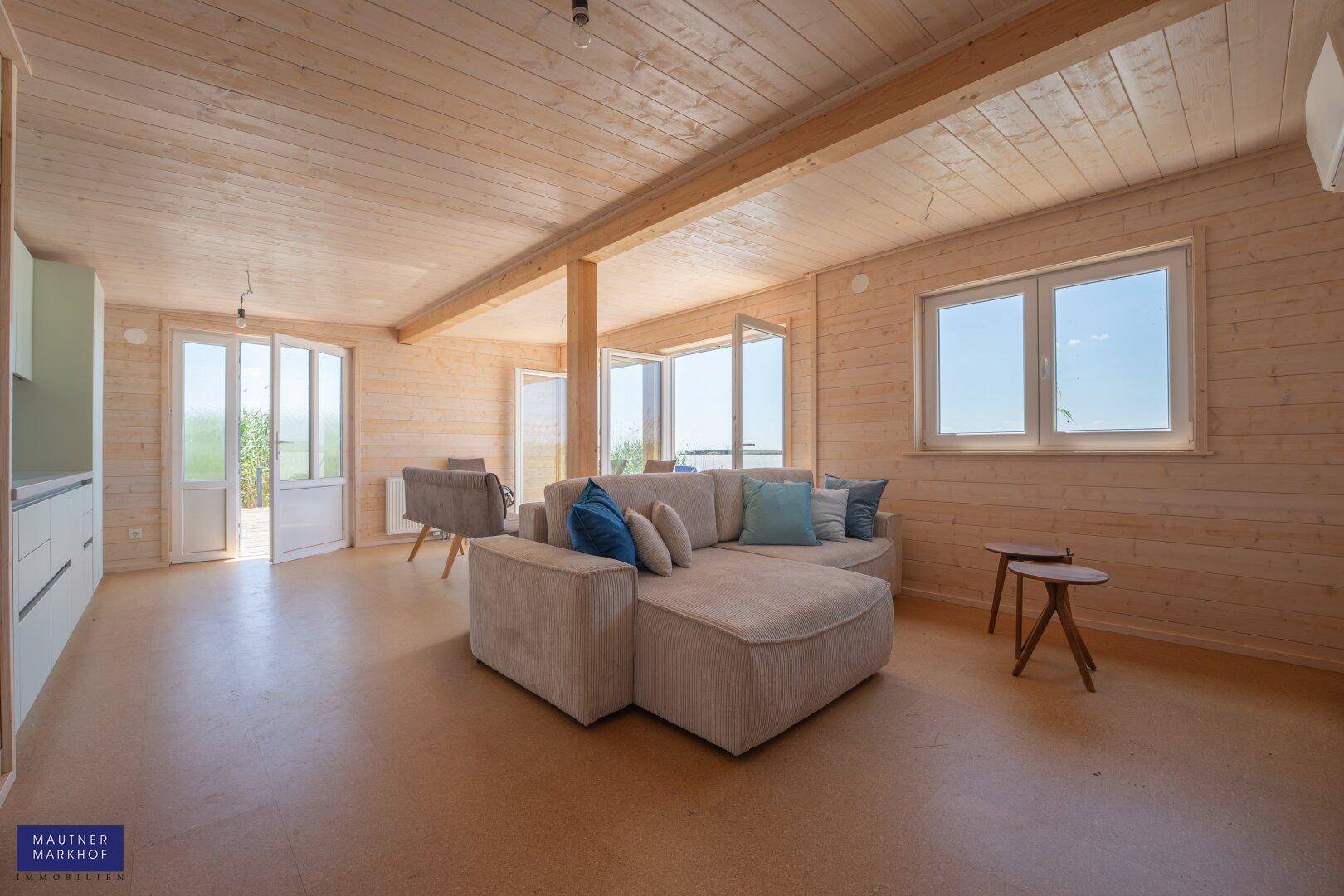 Helles Wohnzimmer mit Holzwänden, Holzbalken und einer beigen Eckcouch.