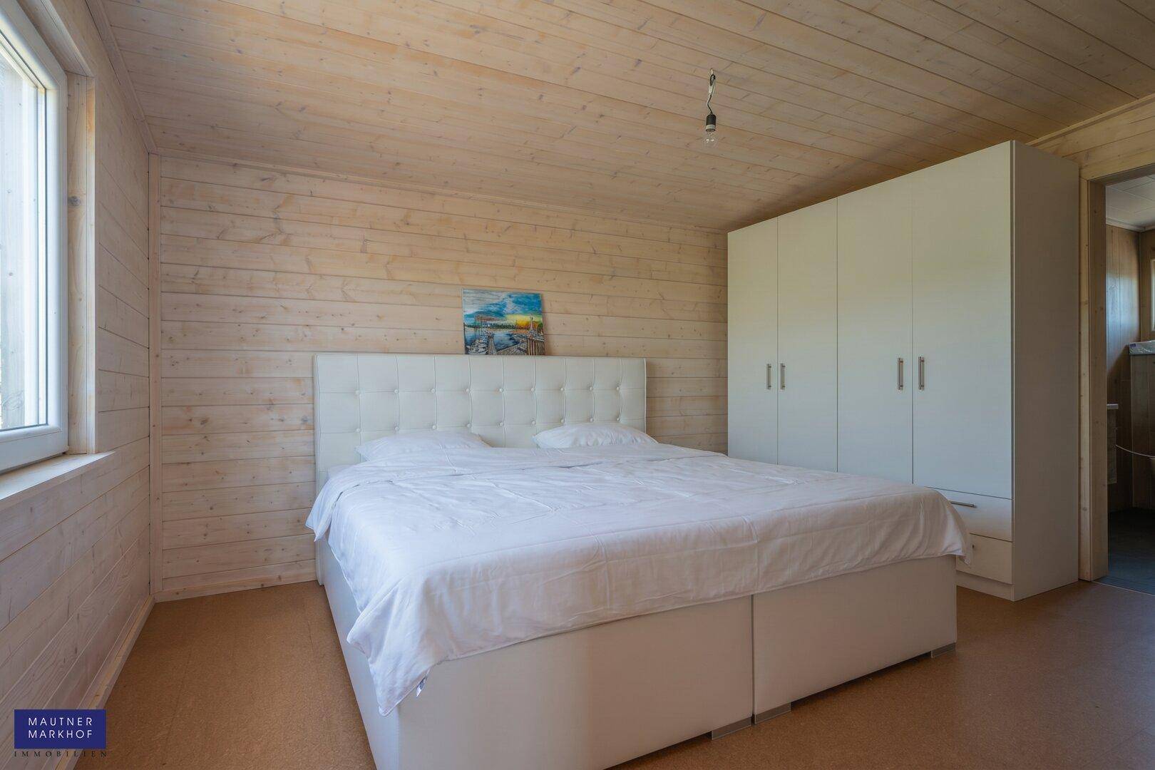 Helles Schlafzimmer mit Holzwänden, Doppelbett und weißem Kleiderschrank.